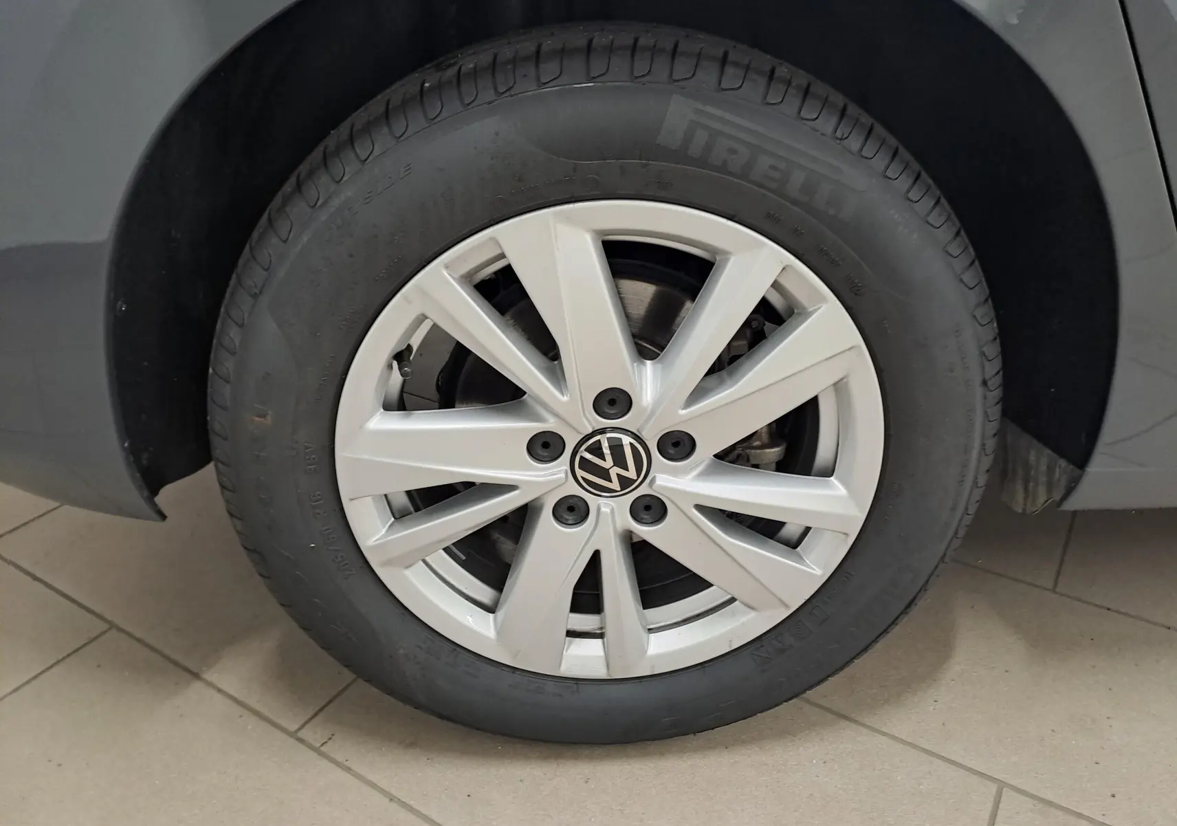 Gros plan sur la roue avant gauche du Volkswagen Touran gris Dauphin, mettant en valeur la jante alliage et le logo VW central.