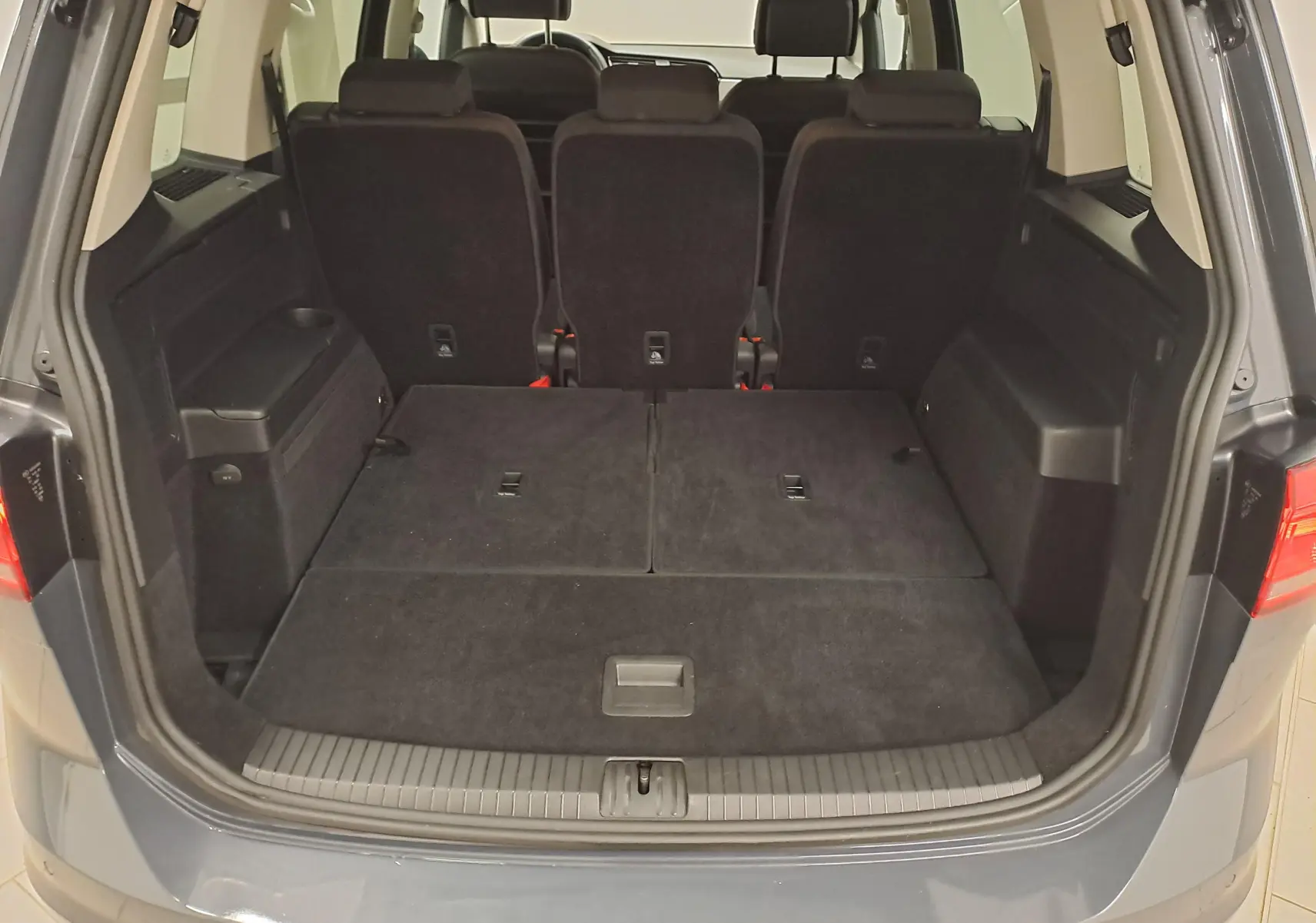 Vue arrière du coffre ouvert du Volkswagen Touran gris Dauphin 2024 avec sièges rabattus et grand espace de chargement.