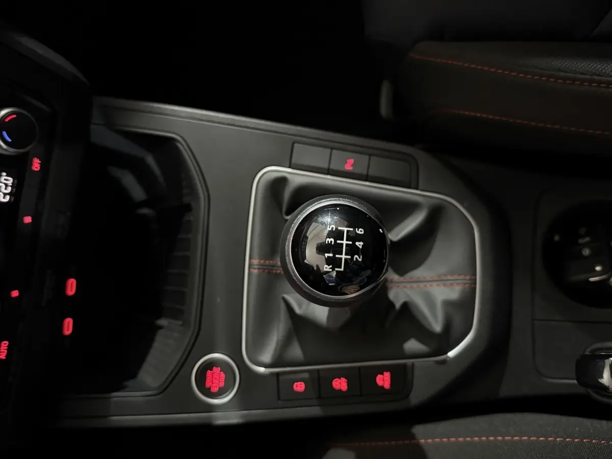 Gros plan sur le levier de vitesses manuel noir avec surpiqûres rouges dans une SEAT Ibiza 1.0 TSI 110 FR gris foncé, intérieur sombre.