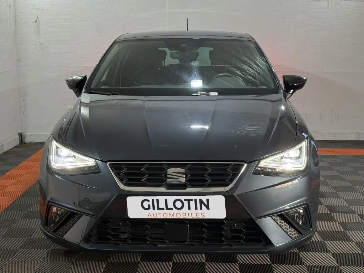 Vue frontale d'une SEAT Ibiza 1.0 TSI 110 FR gris foncé avec phares LED allumés en intérieur.