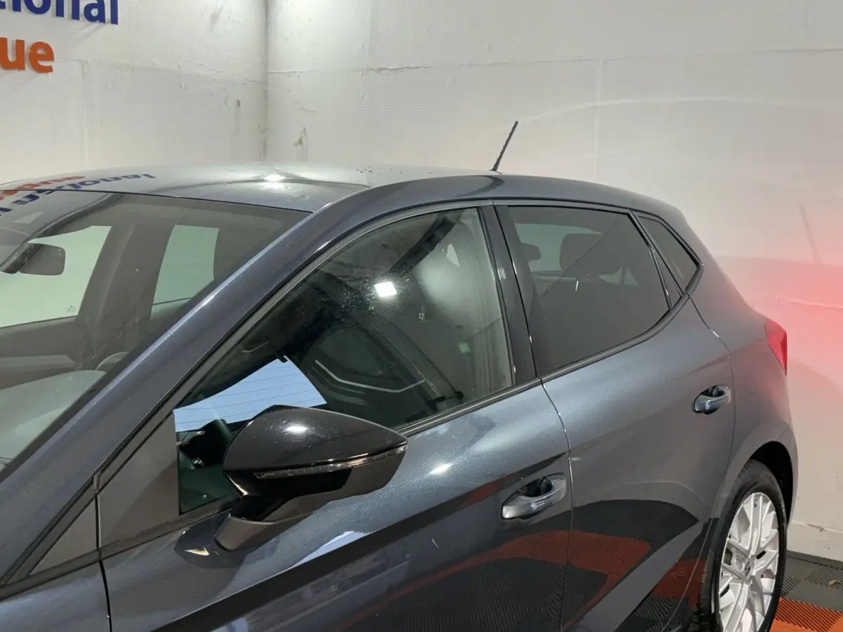 Vue côté gauche arrière d'une SEAT Ibiza gris foncé 2024 avec rétroviseur noir et jantes argentées.