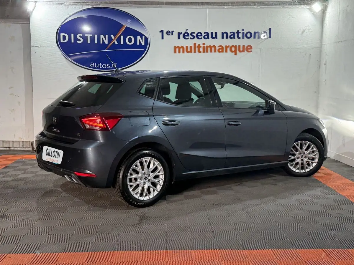 Vue 3/4 arrière droite d'une SEAT Ibiza 1.0 TSI 110 FR gris foncé, avec jantes alliage et feux LED distinctifs.
