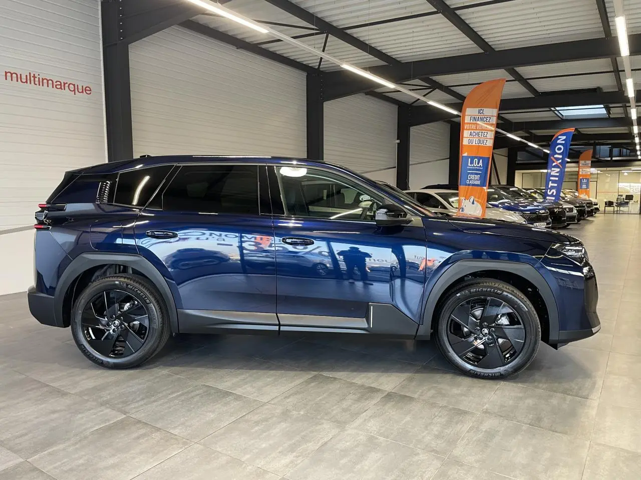 Vue latérale gauche d'un Citroën C5 Aircross bleu Azul avec jantes alliage noires en showroom.