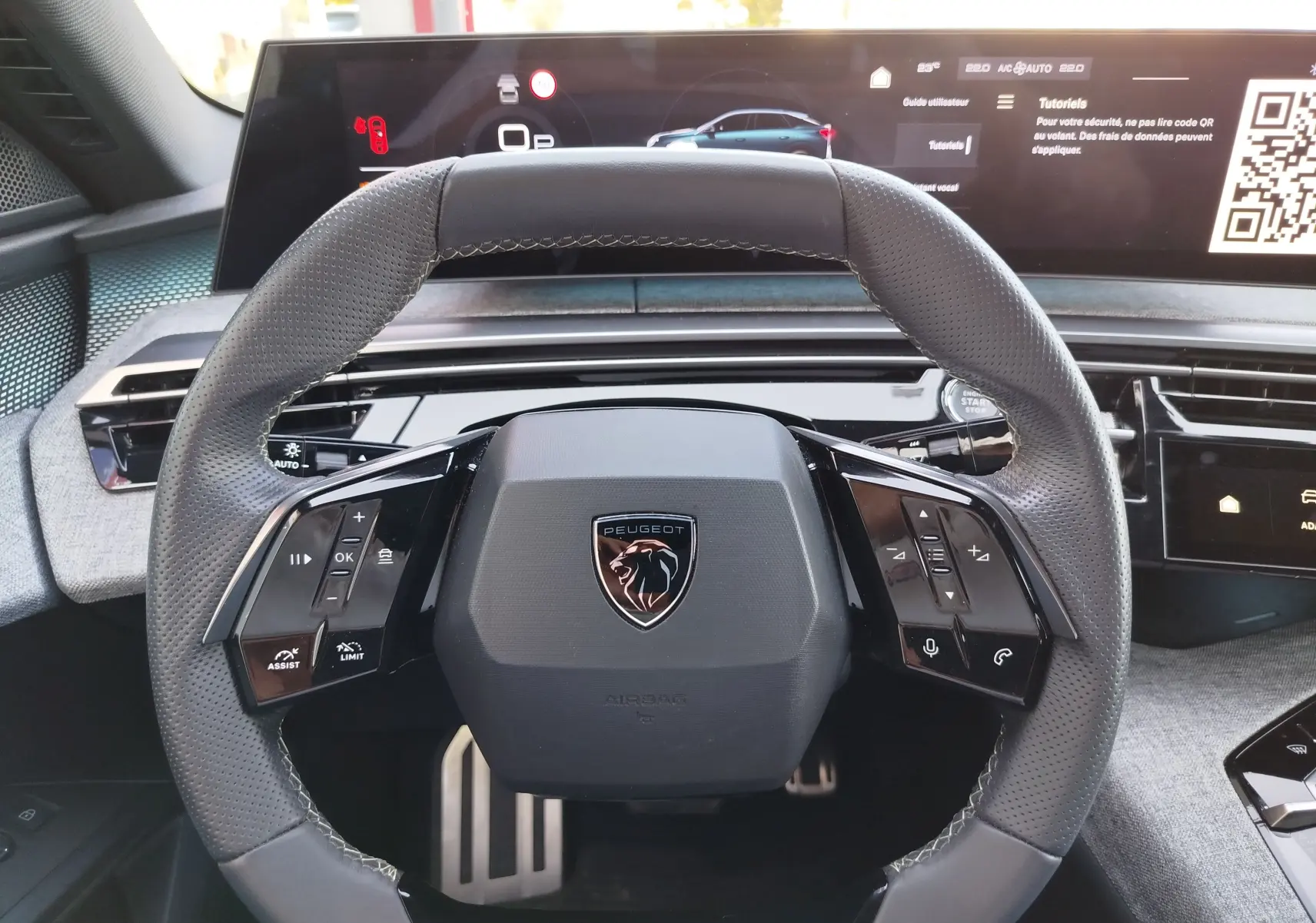Vue rapprochée du volant multifonction noir avec logo Peugeot, tableau de bord numérique et commandes tactiles visibles.