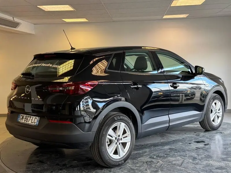 Vue 3/4 arrière droite d'un Opel Grandland noir Karbon métallisé avec jantes alu dans un intérieur lumineux.