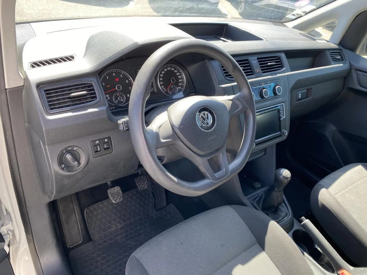 Intérieur du Volkswagen Caddy blanc, vue côté conducteur, volant, tableau de bord et levier de vitesse manuel visibles.