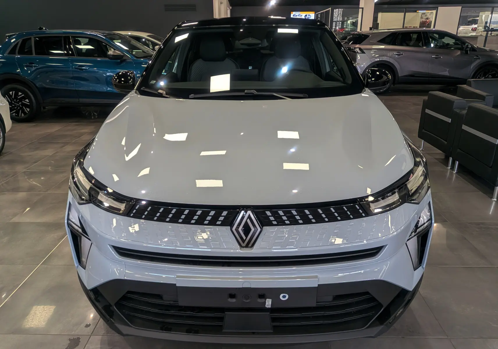 Vue avant d'un Renault Captur 2025 gris Rafale avec toit noir, éclairage LED et calandre moderne en showroom.