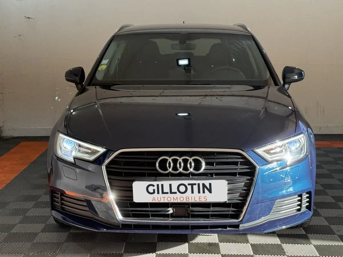 Vue avant d'une Audi A3 2.0 TDI 150 Business Line bleu métallisé avec phares allumés en intérieur.