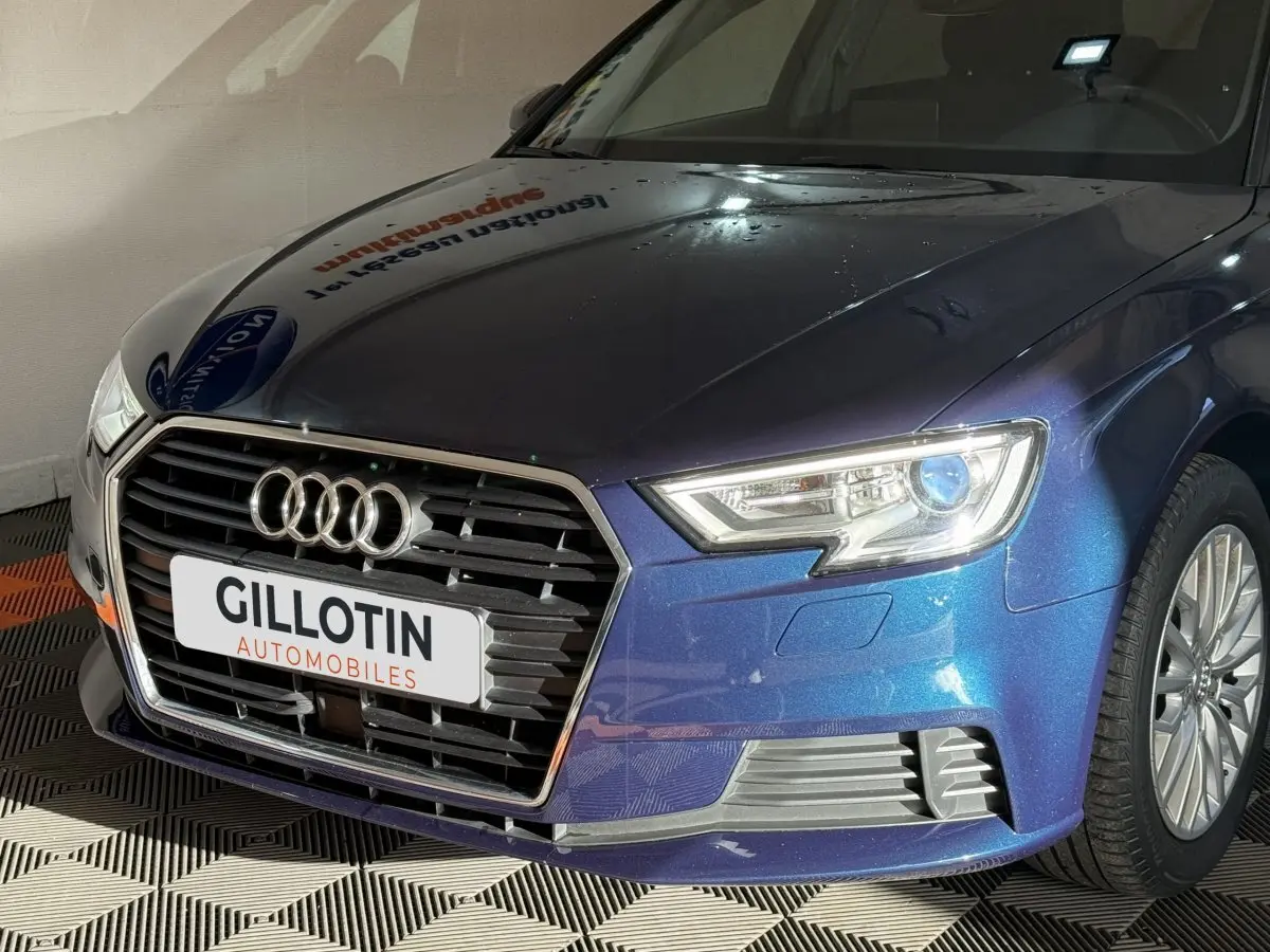 Vue 3/4 avant droit d'une Audi A3 2.0 TDI Business Line bleu métallisé avec phares LED et calandre chromée.
