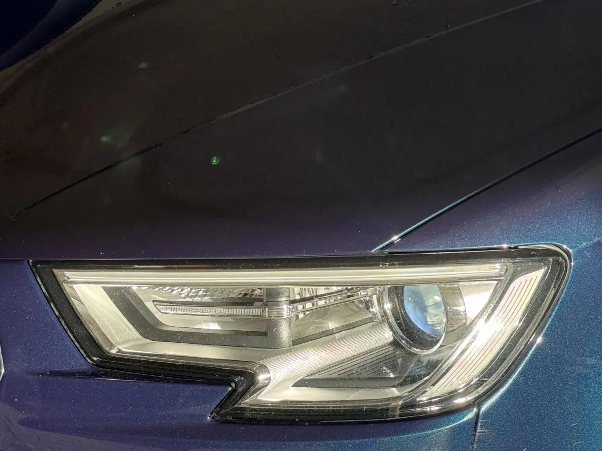 Gros plan sur le phare avant droit d’une Audi A3 bleu métallisé, mettant en valeur son design LED distinctif.