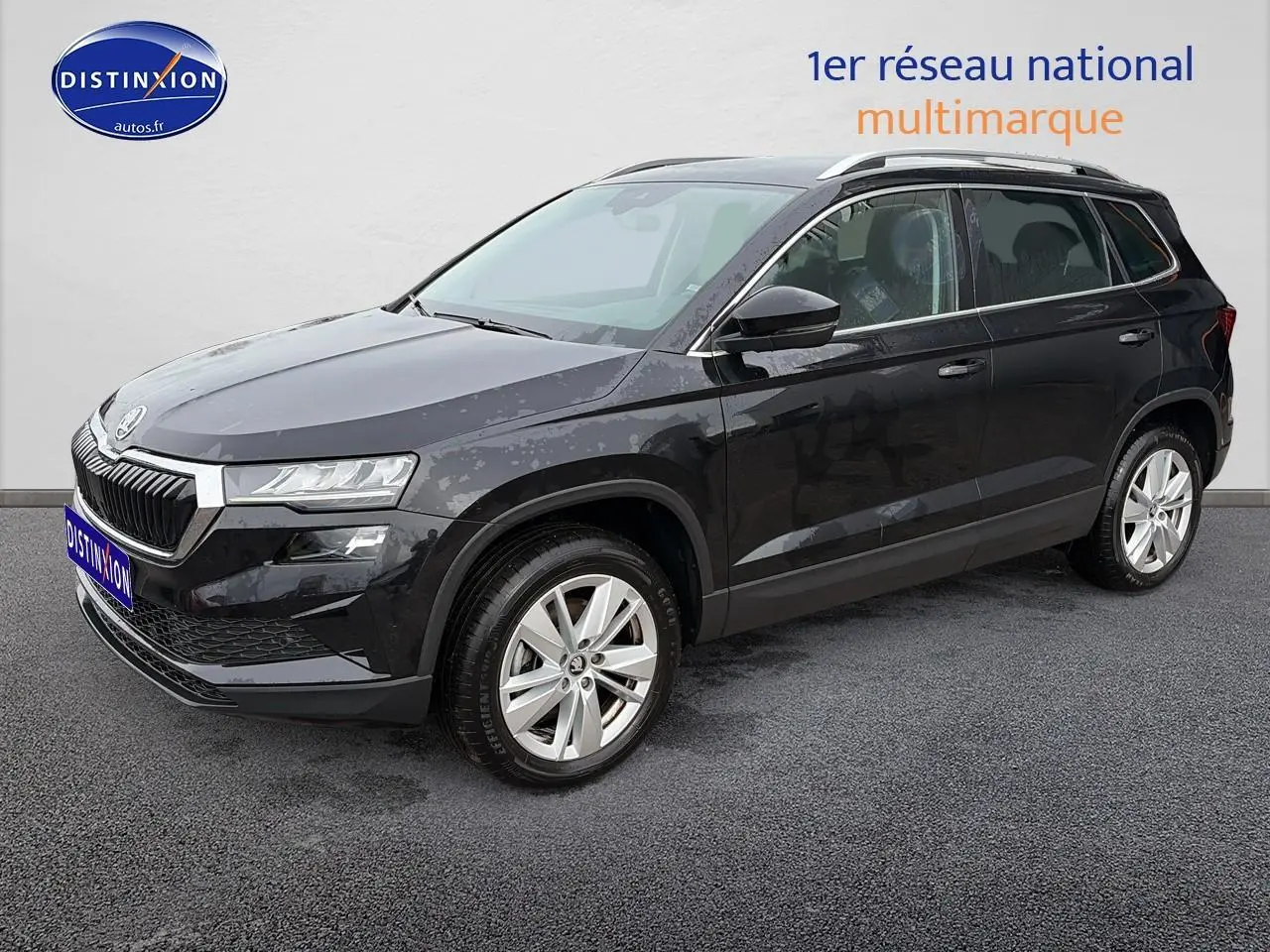 Vue 3/4 avant d’un Skoda Karoq noir 2025 avec jantes alu et barres de toit visibles sur fond neutre.