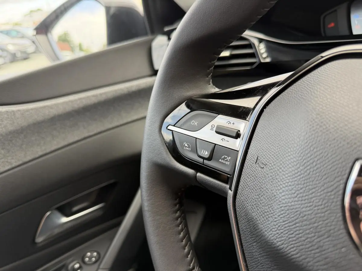 Gros plan sur le volant noir avec commandes intégrées côté gauche et partie de la porte intérieure grise d’une Peugeot 308 SW rouge.