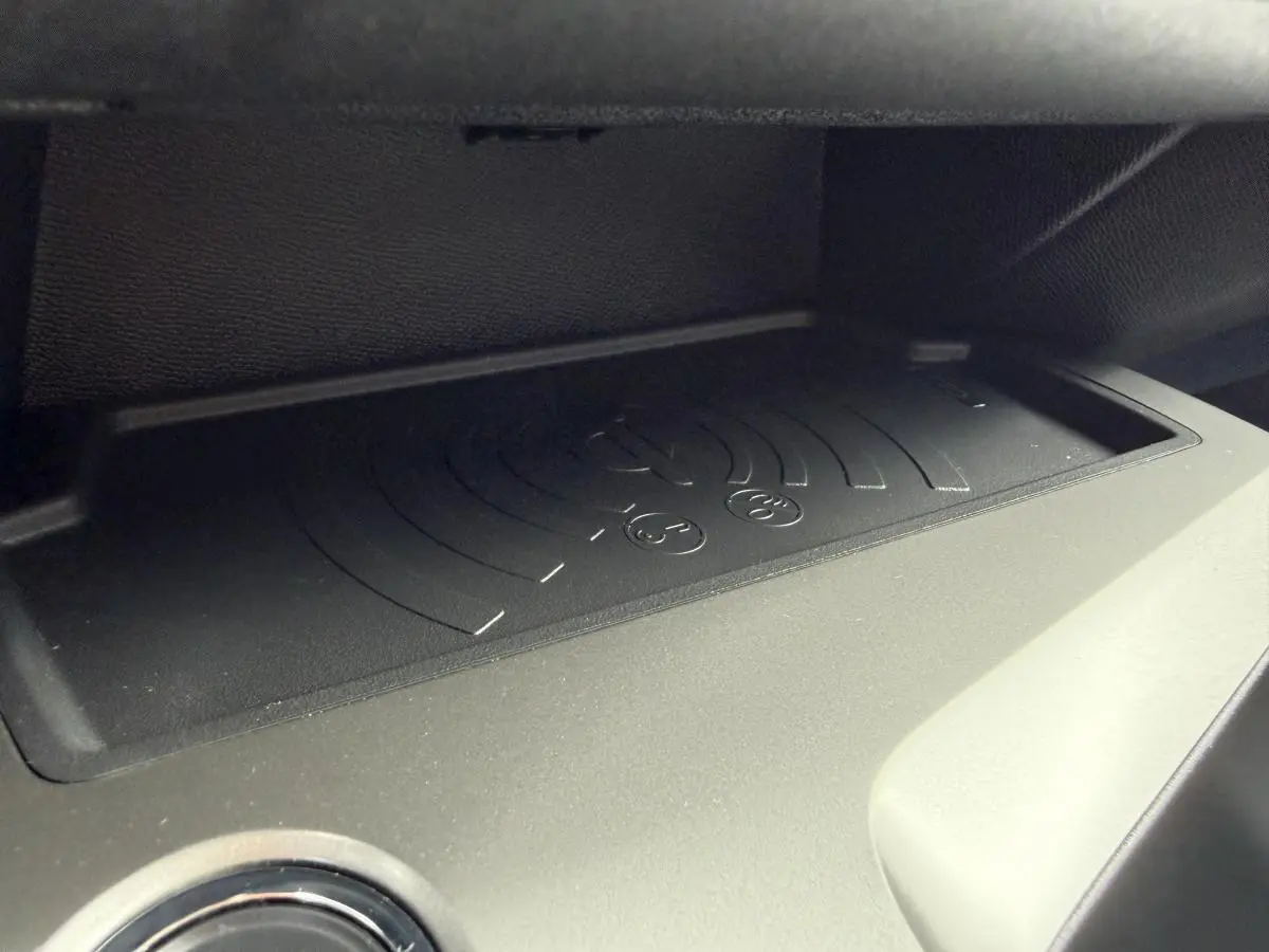 Gros plan sur le chargeur sans fil noir intégré dans l'habitacle de la Peugeot 308 SW 1.6 PHEV rouge, année 2024.