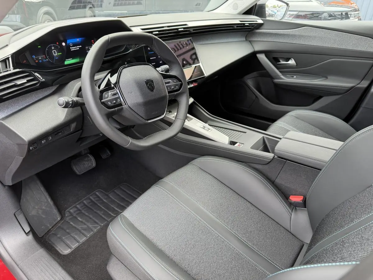 Intérieur avant droit de la Peugeot 308 SW 2024, avec tableau de bord numérique et sellerie tissu gris à surpiqûres bleues.