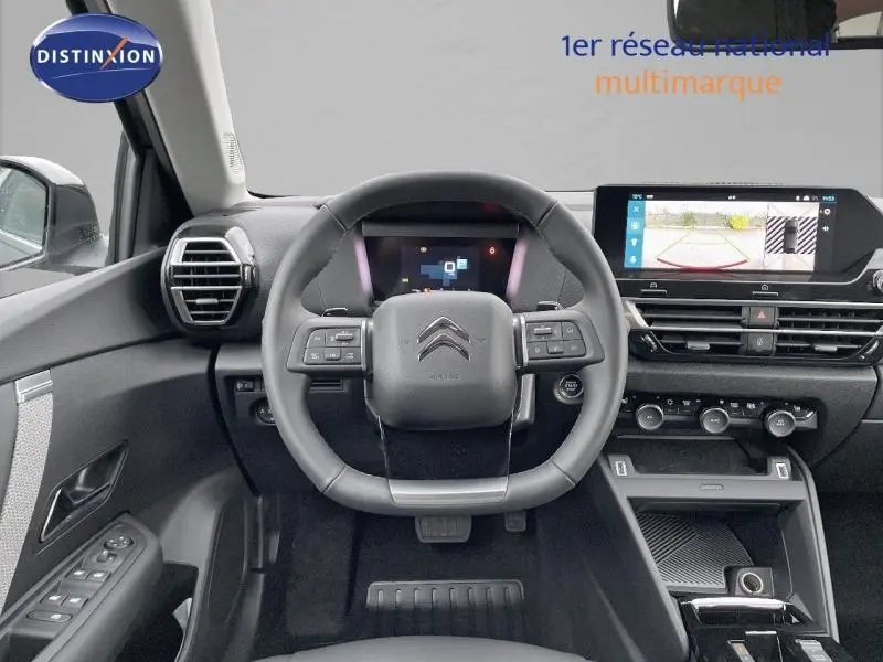 Vue intérieure centrée sur le volant cuir et tableau de bord numérique du Citroën C4 gris 2024 avec écran tactile affichant la caméra de recul.