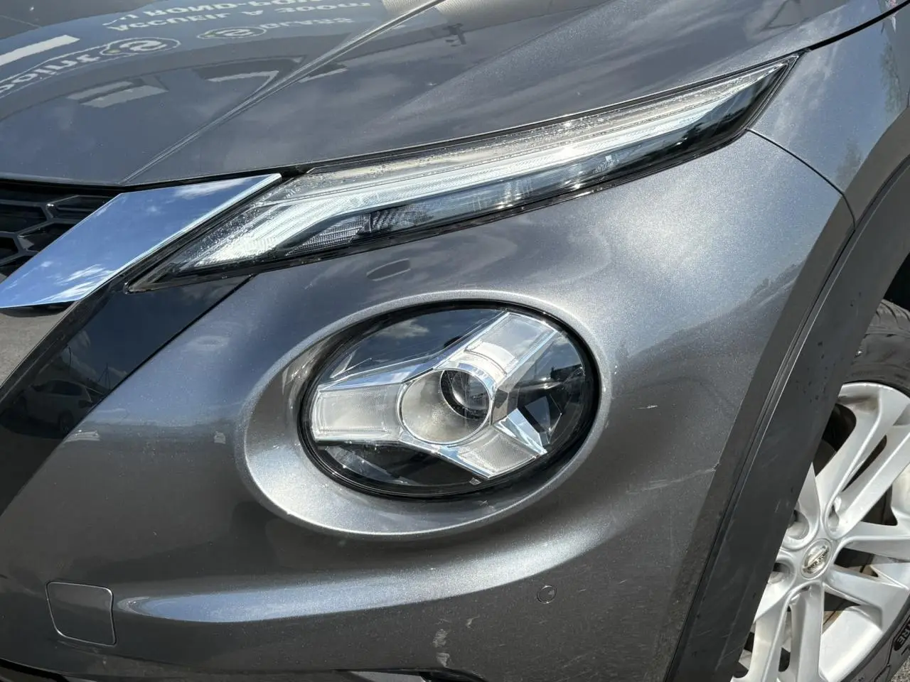 Gros plan sur le phare avant droit du Nissan Juke 2024 gris Dark Metal, mettant en valeur le design LED et la jante alliage 17 pouces.