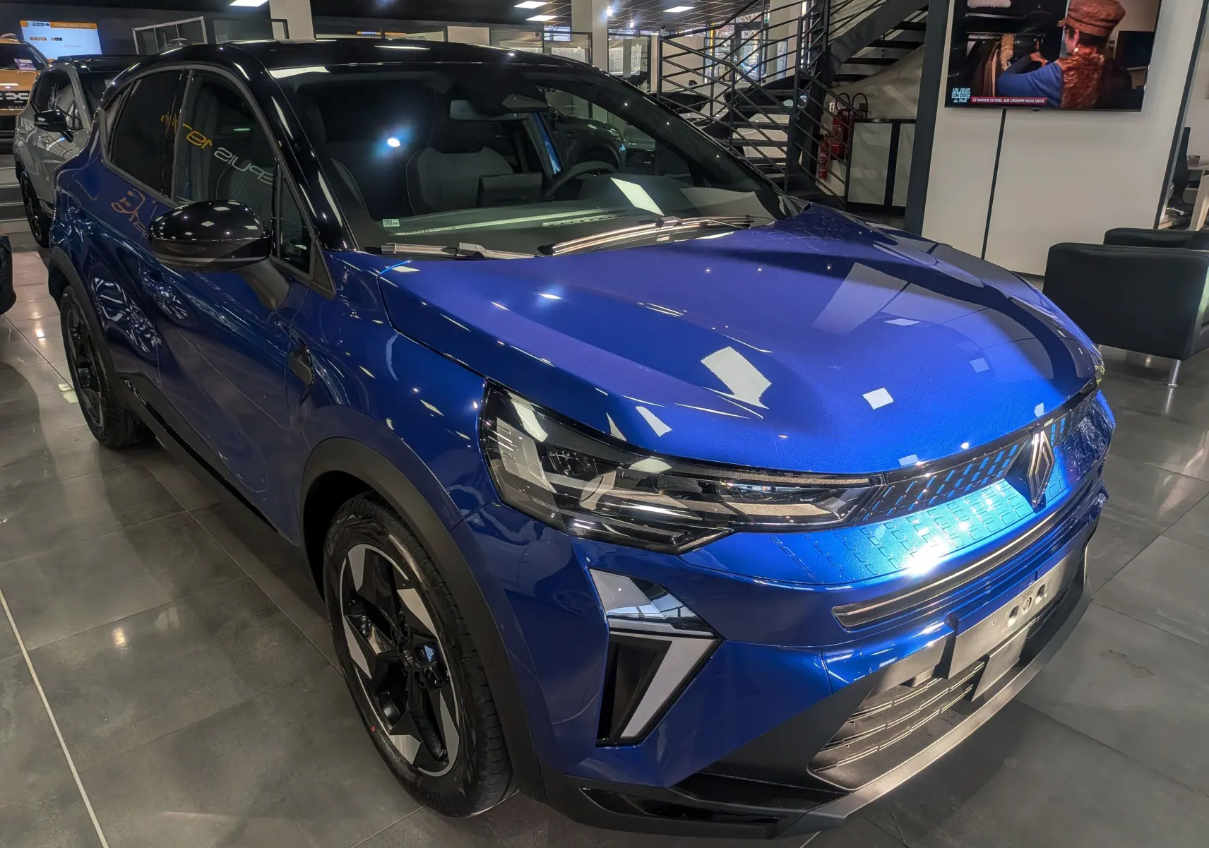 Renault Captur 2025 bleu Iron avec toit noir, vue 3/4 avant mettant en valeur ses phares LED et jantes biton.