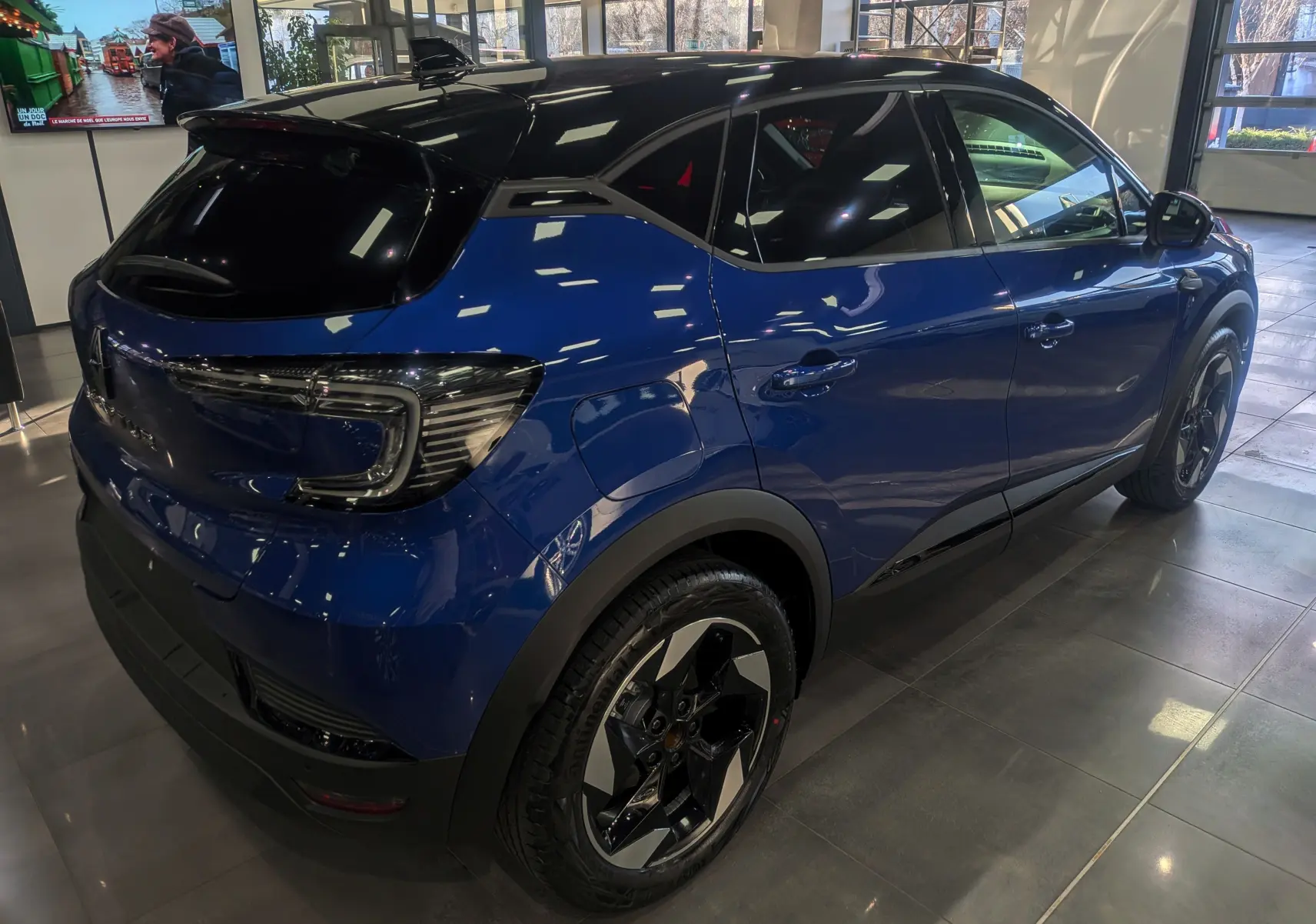 Vue 3/4 arrière droite du Renault Captur 2025 bleu Iron avec toit noir et jantes biton dans un showroom.