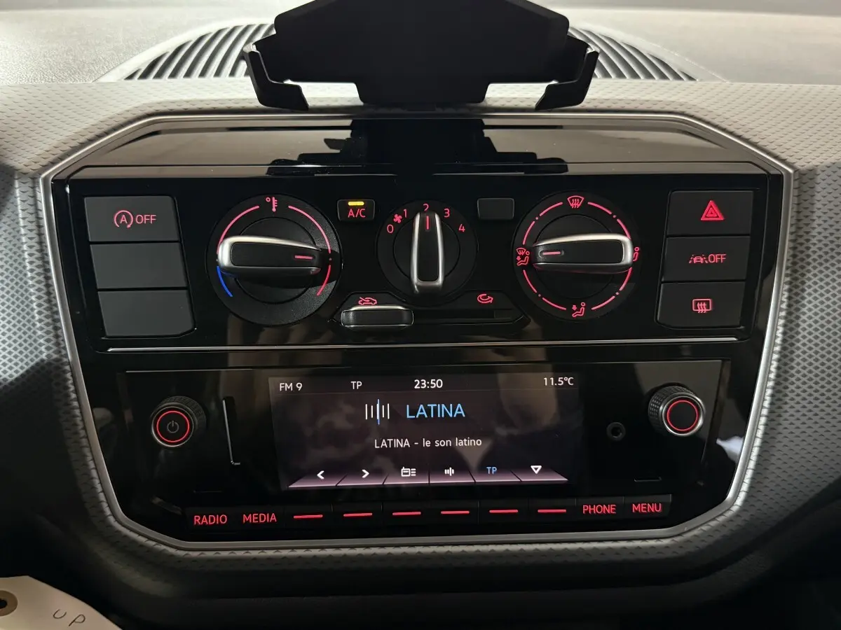 Vue rapprochée du tableau de bord noir du Volkswagen Up gris foncé, montrant les commandes de climatisation et l’écran multimédia allumé.