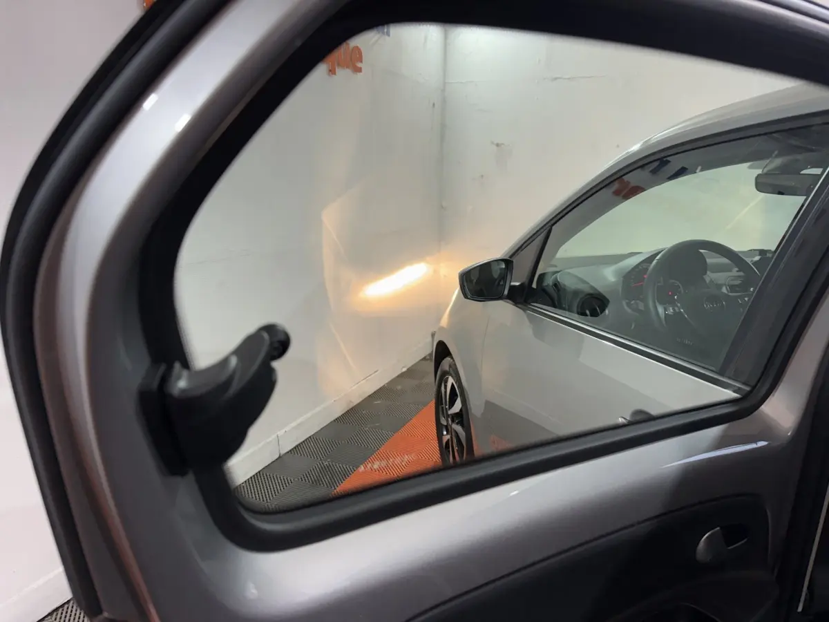 Vue partielle côté droit d’une Volkswagen Up gris foncé, avec rétroviseur extérieur et intérieur visibles en stationnement.