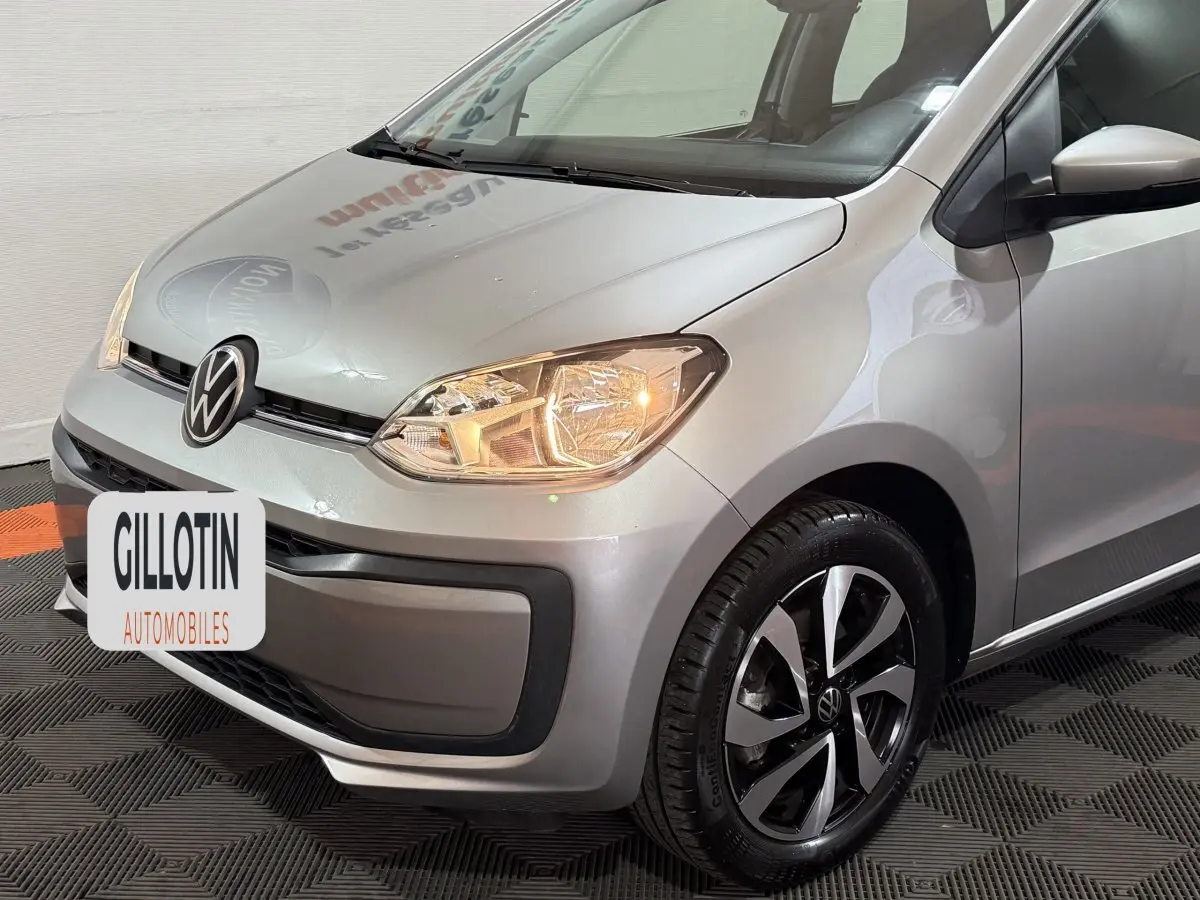 Vue 3/4 avant droit d'une Volkswagen Up gris foncé avec phares allumés et jantes alliage distinctives.