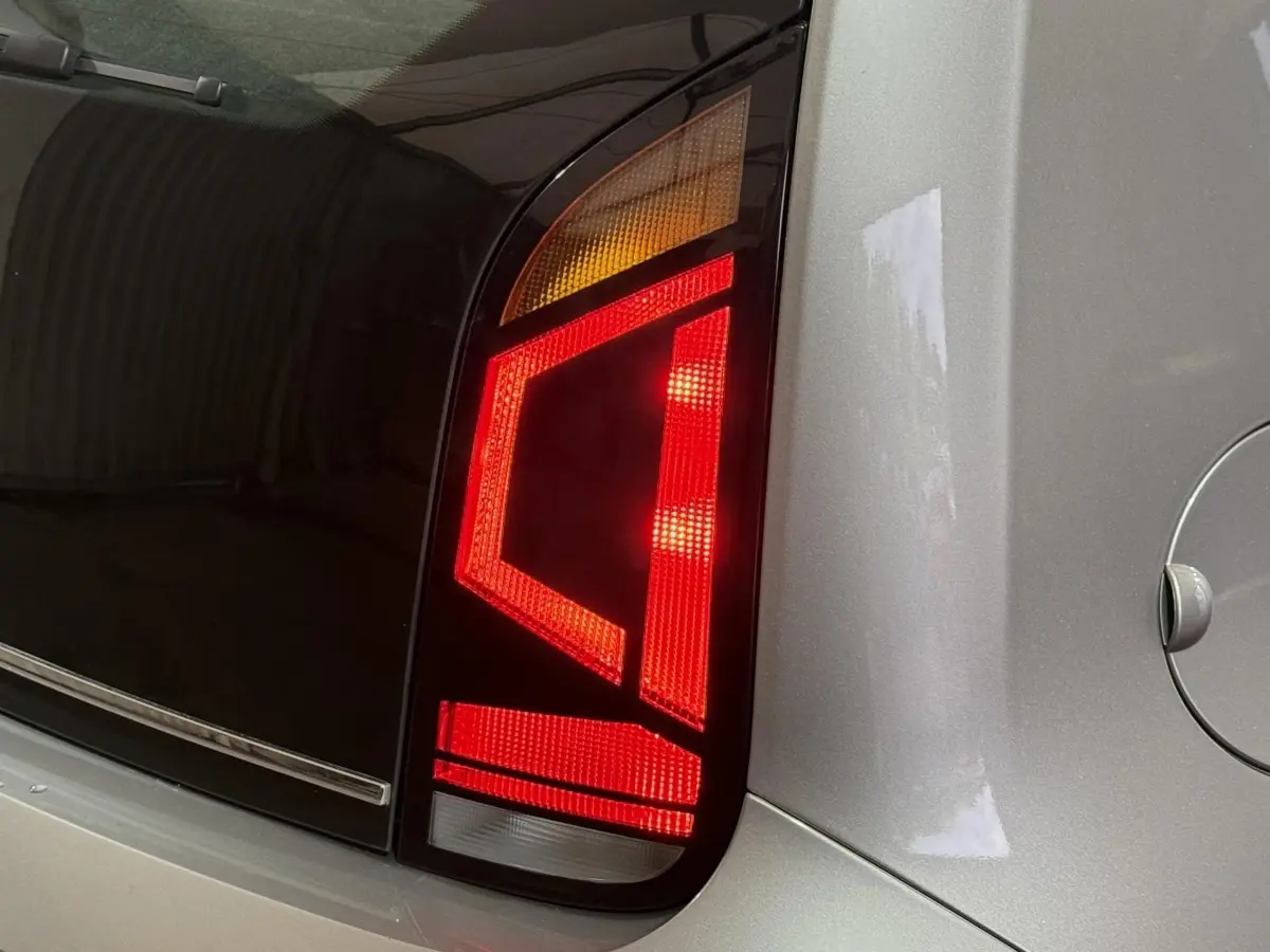 Gros plan sur le feu arrière droit rouge et orange d'une Volkswagen Up gris foncé, avec la trappe à carburant visible.