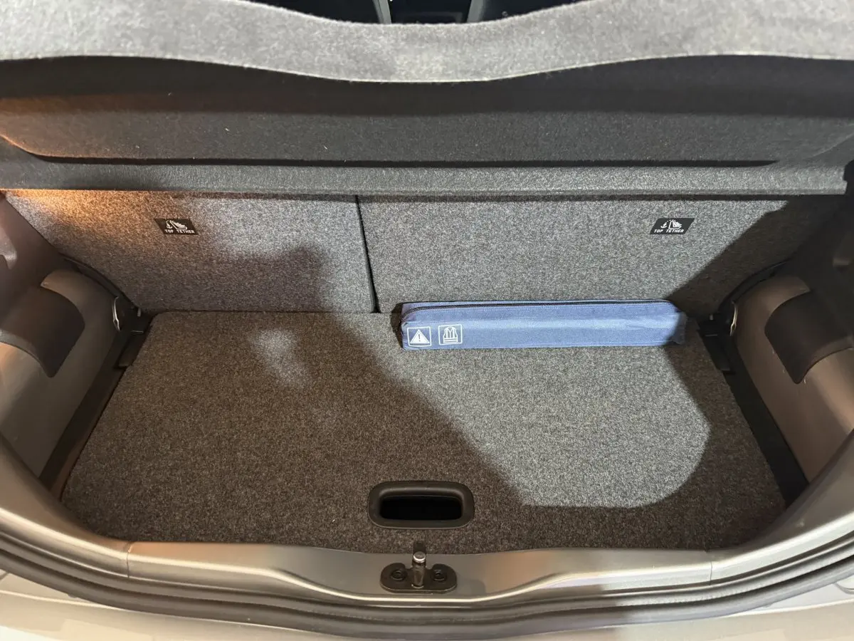 Coffre ouvert d’une Volkswagen Up gris foncé, vue de dessus montrant la moquette et un kit de sécurité bleu.