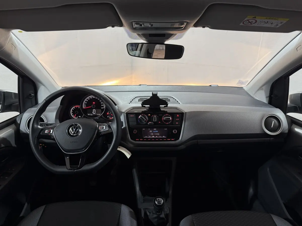 Vue intérieure frontale du tableau de bord gris clair et noir du Volkswagen Up 1.0 65 Active avec volant cuir et boîte manuelle.