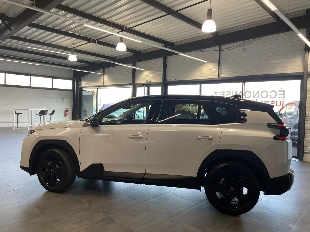 Vue latérale gauche du Citroën C5 Aircross blanc Okenite avec toit noir et jantes alliage noires en intérieur showroom.