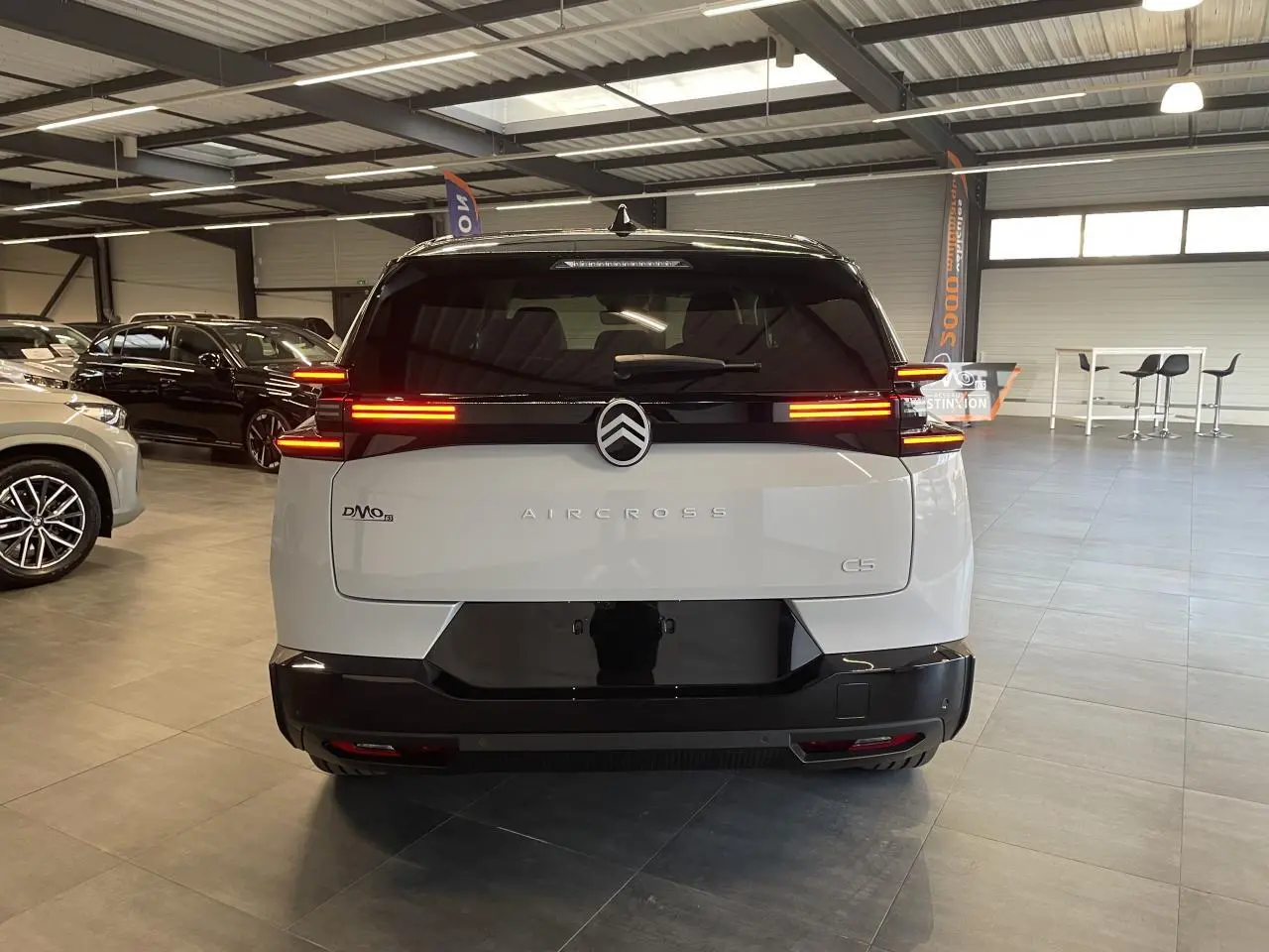 Vue arrière d'un Citroën C5 Aircross blanc Okenite avec toit noir et feux arrière LED allumés en intérieur showroom.