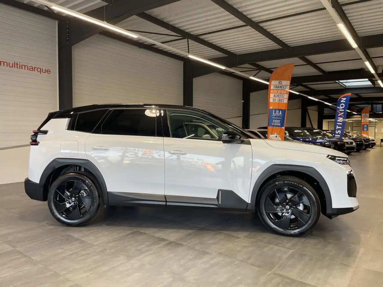 Vue latérale droite du Citroën C5 Aircross blanc Okenite avec toit noir et jantes alliage noires en intérieur showroom.
