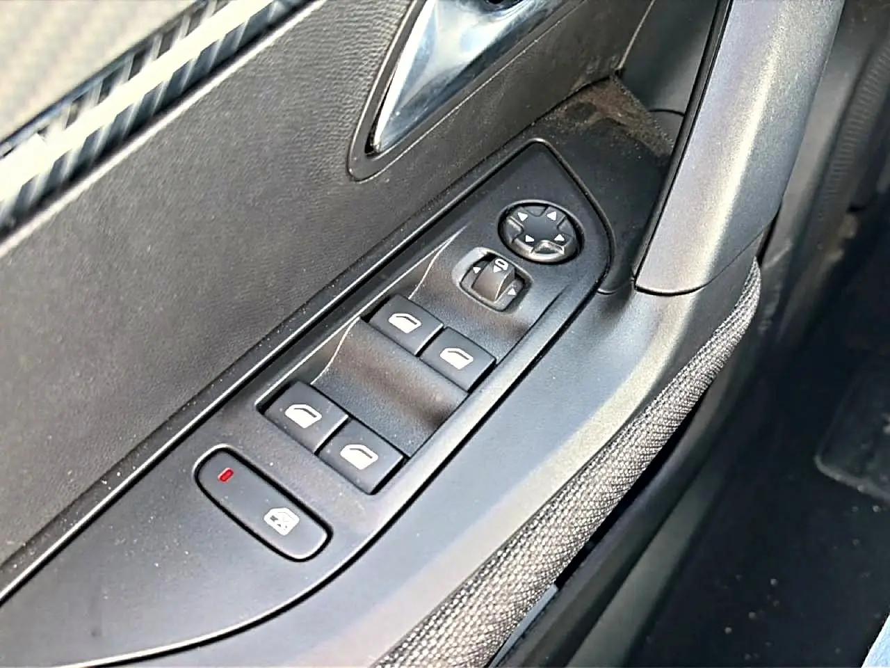Gros plan sur la commande des vitres électriques côté gauche, avec tissu gris et plastique noir dans l’habitacle Peugeot 2008.