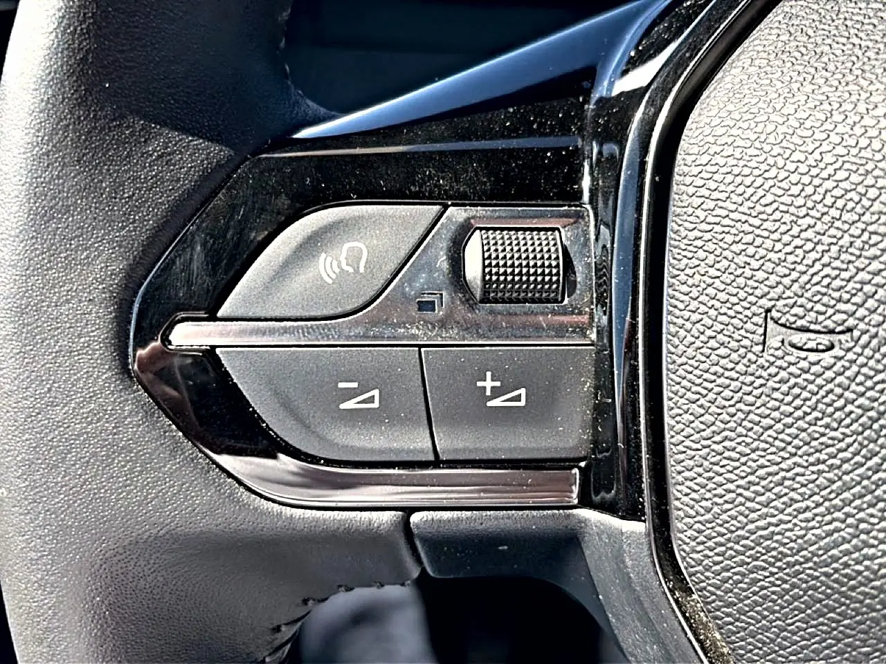 Gros plan sur les commandes de volume et appel mains-libres du volant noir du Peugeot 2008 gris 2025.