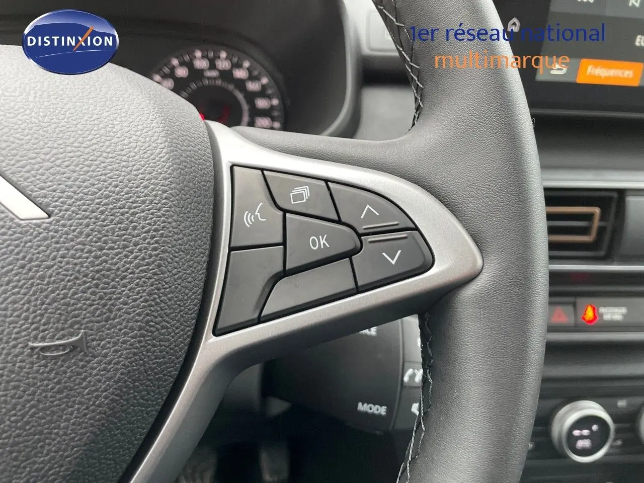 Gros plan sur le volant côté gauche du Dacia Jogger noir nacré, avec commandes multifonctions visibles et tableau de bord flou.