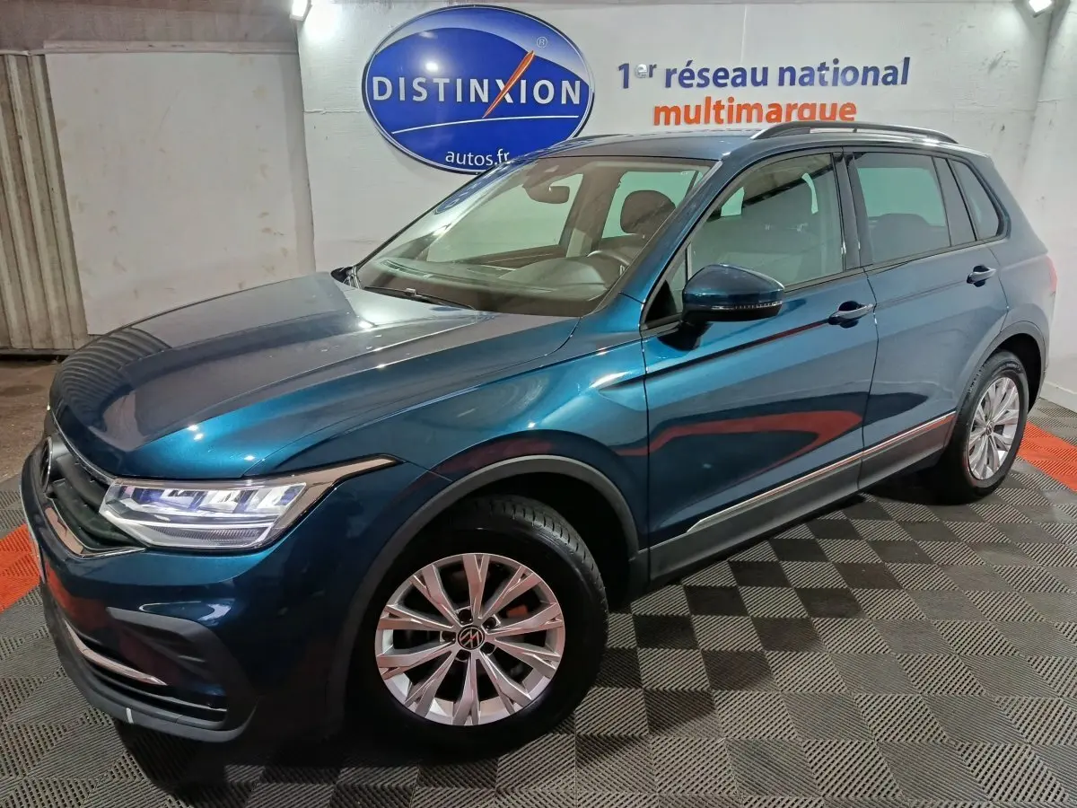 Volkswagen Tiguan bleu en 3/4 avant droit, avec jantes alliage et phares LED visibles en intérieur showroom.