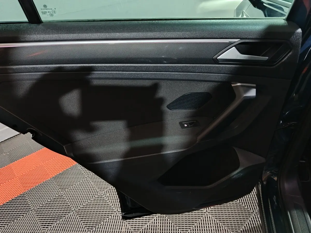 Vue intérieure de la porte arrière droite du Volkswagen Tiguan bleu, avec poignée et commande de vitre électrique.