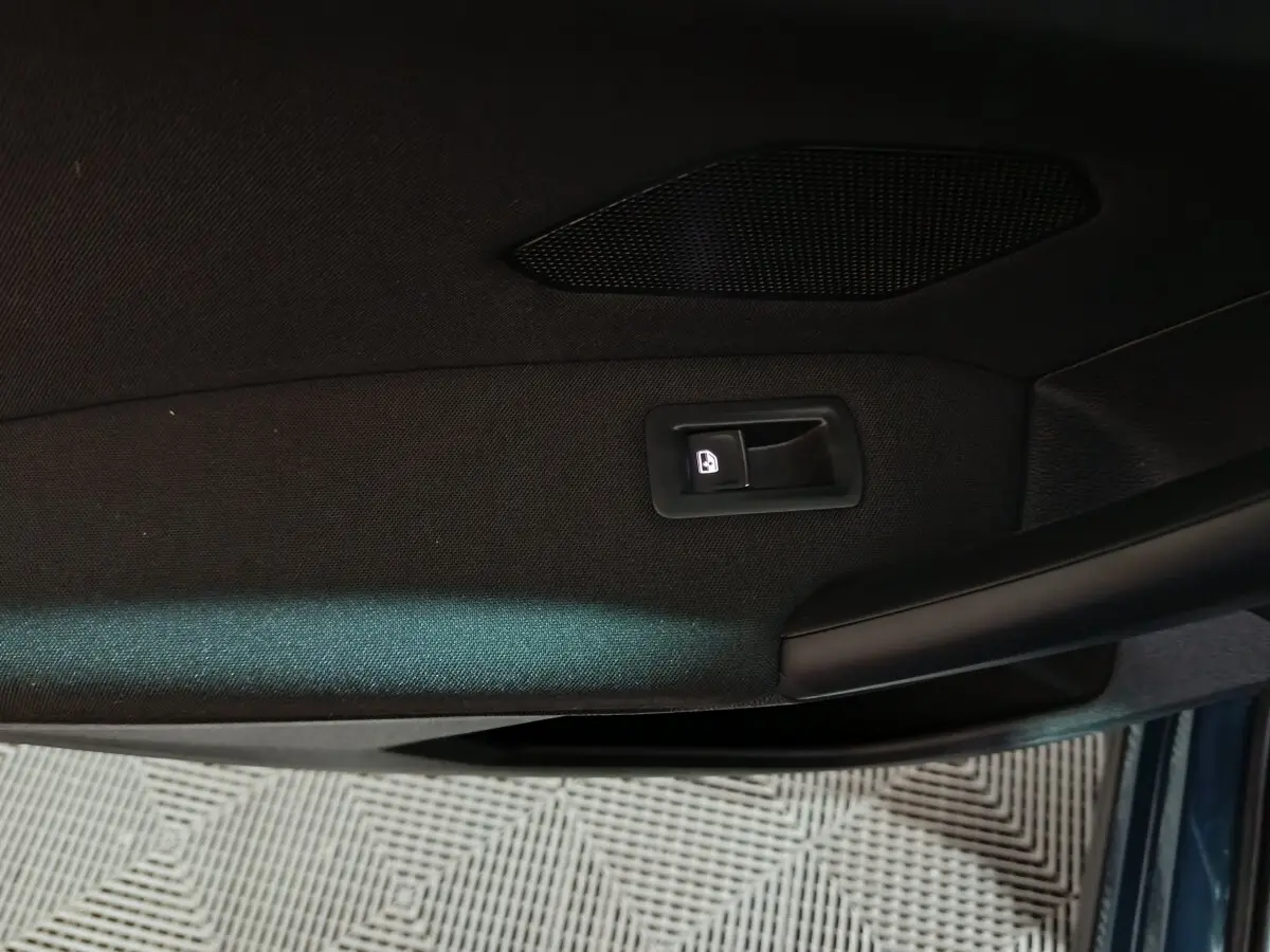 Détail de la poignée intérieure de porte côté gauche du Volkswagen Tiguan bleu, avec bouton de verrouillage éclairé.