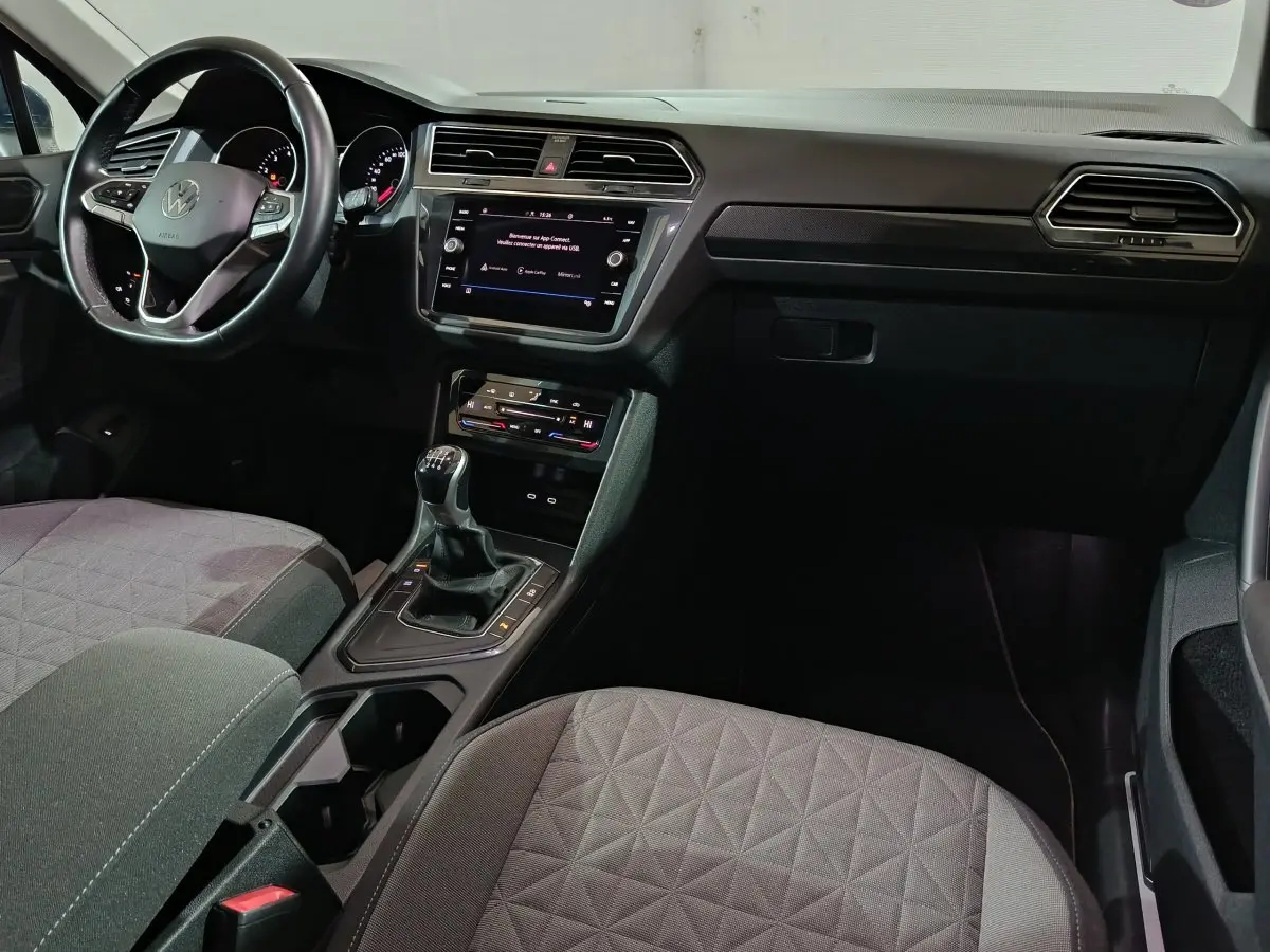 Vue intérieure côté conducteur du Volkswagen Tiguan 2021 avec volant cuir, tableau de bord noir et levier de vitesses manuel.