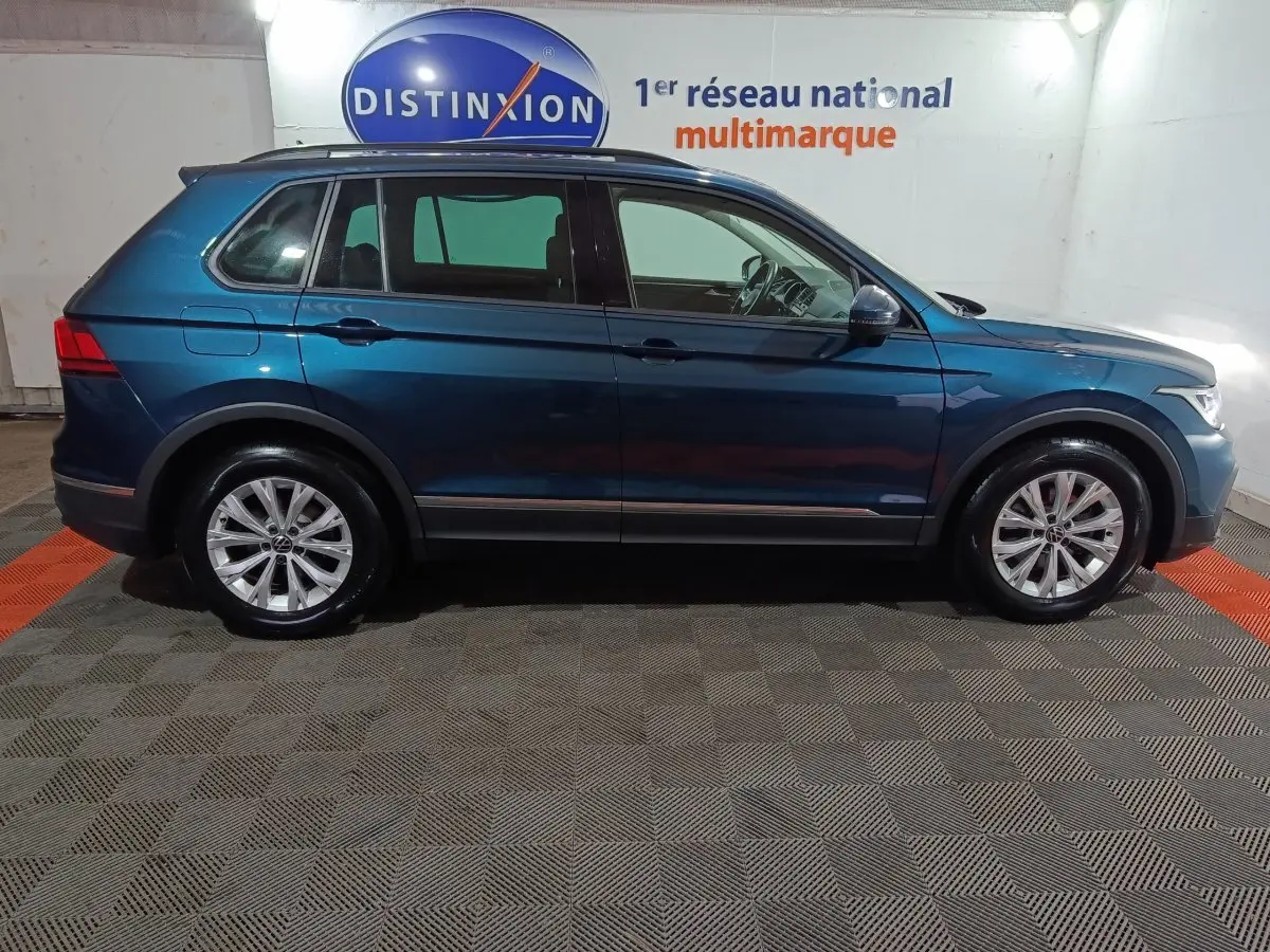 Vue de profil côté gauche d’un Volkswagen Tiguan bleu 2021 garé en intérieur sur sol carrelé.