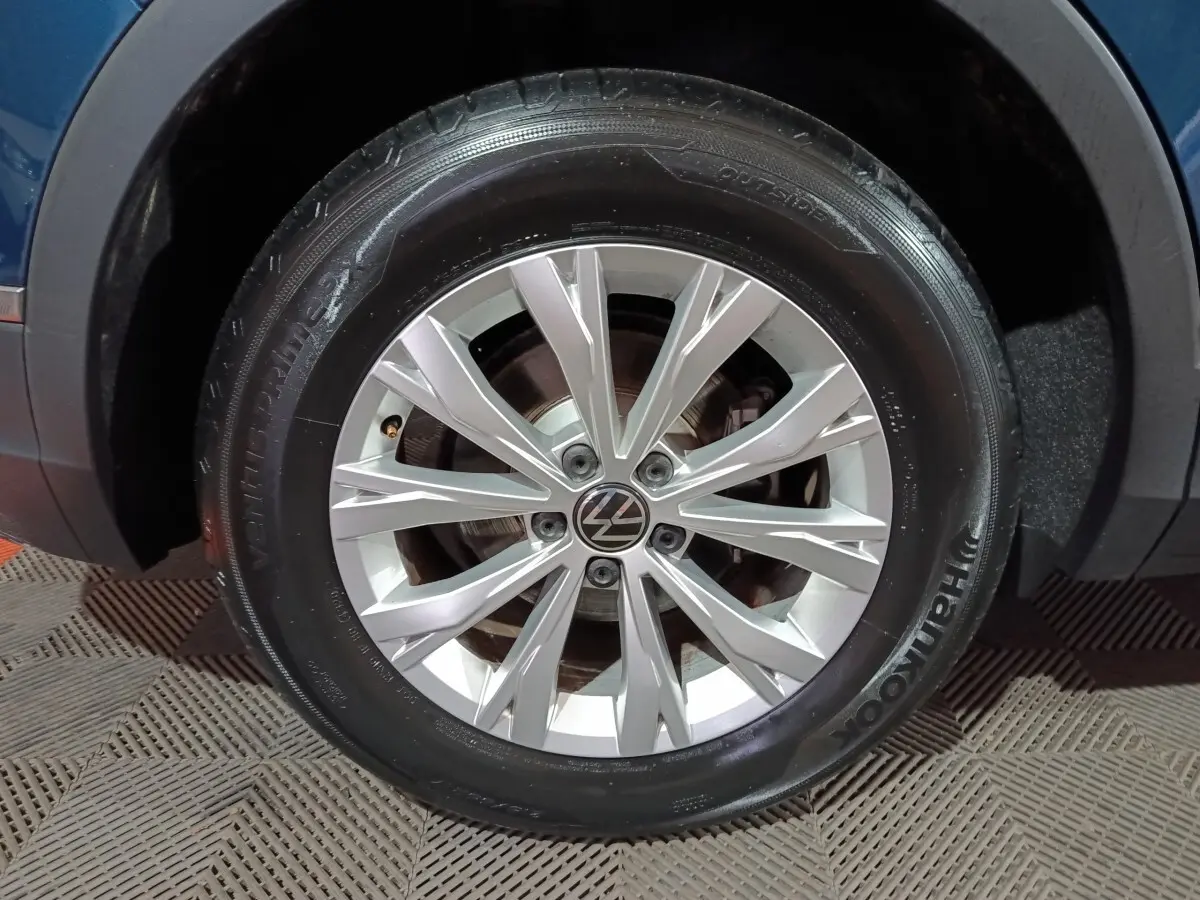 Gros plan sur la roue avant gauche d’un Volkswagen Tiguan bleu, avec jante alliage argentée et logo VW au centre.