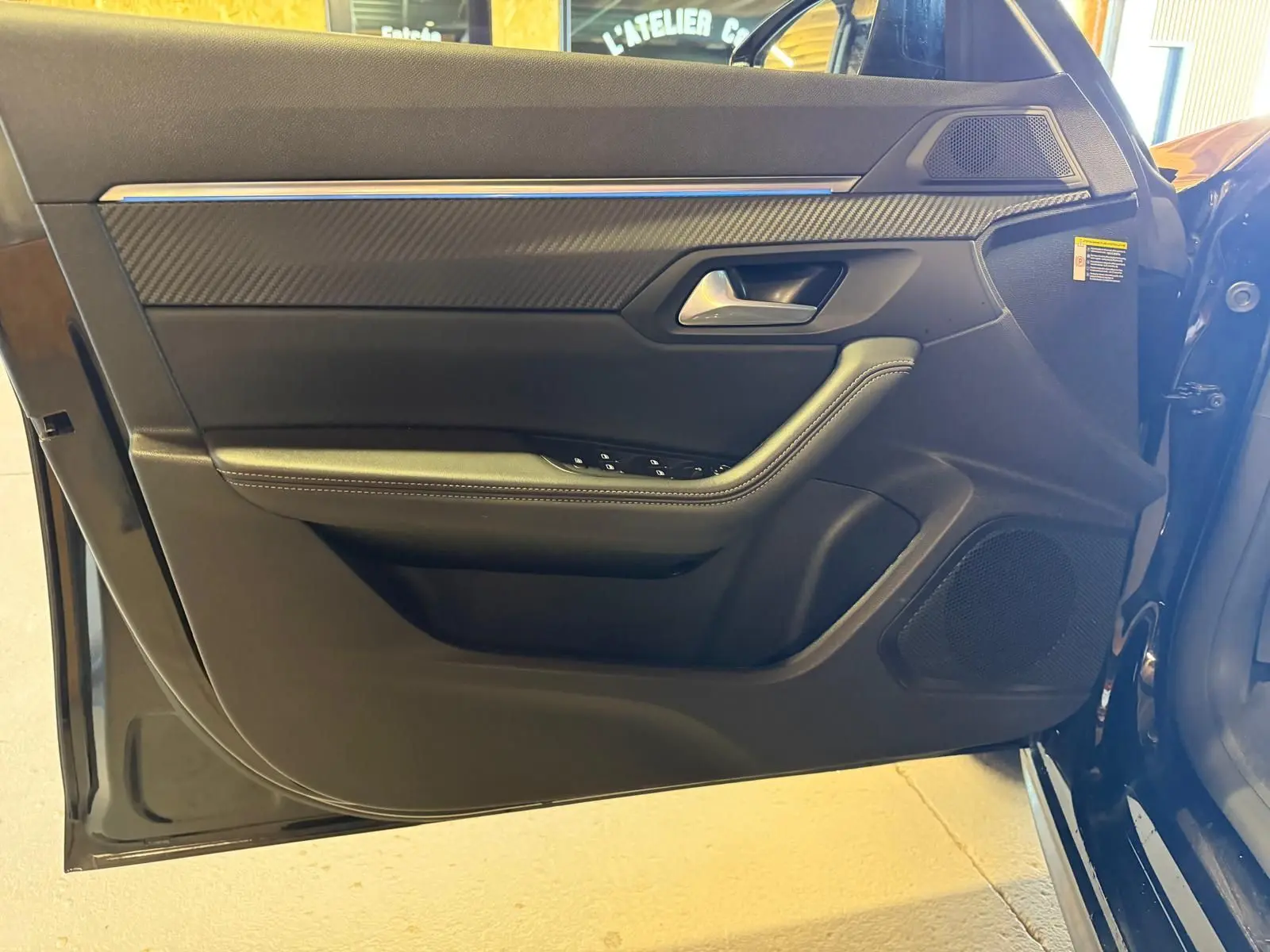 Vue rapprochée de la porte avant gauche noire du Peugeot 508 SW 2024 avec inserts carbone et commandes de lève-vitres.