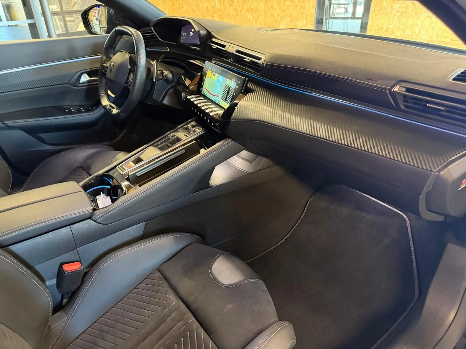 Vue intérieure côté passager du Peugeot 508 SW 2024 noir, avec tableau de bord carbone et éclairage d'ambiance bleu.