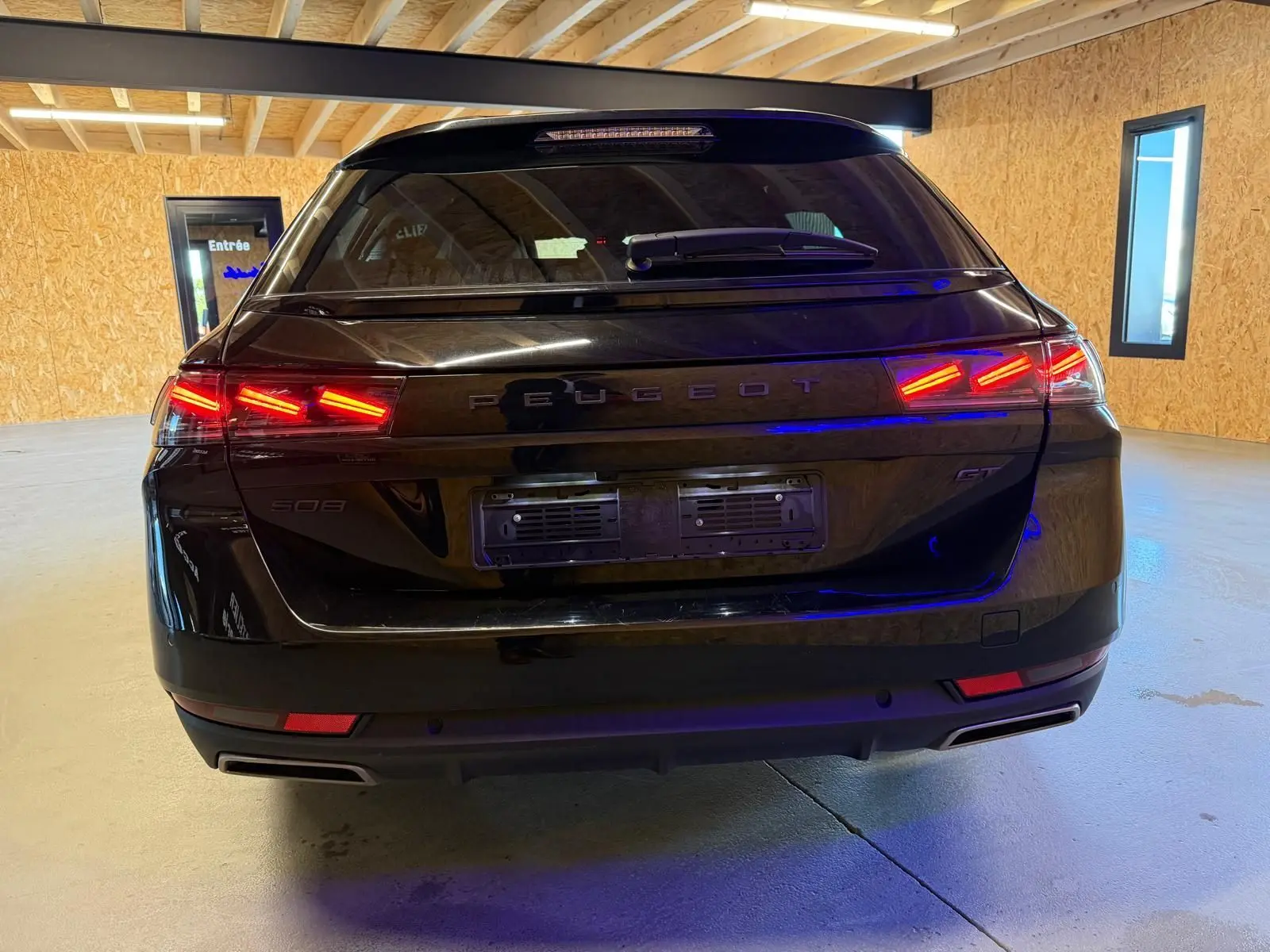 Vue arrière d’un break Peugeot 508 SW noir avec feux LED allumés et badges PEUGEOT et GT visibles.