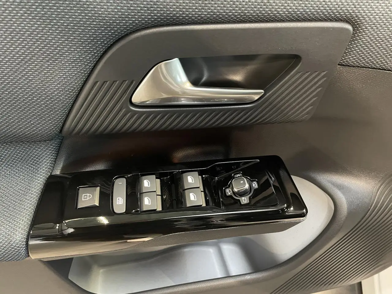 Gros plan sur la commande de lève-vitres et rétroviseurs côté conducteur du Citroën C5 Aircross 2026 noir et gris.
