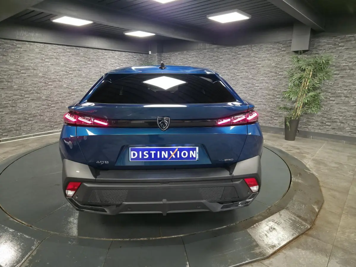 Vue arrière d'une Peugeot 408 hybride rechargeable bleu métallisé avec feux arrière LED allumés dans un showroom.
