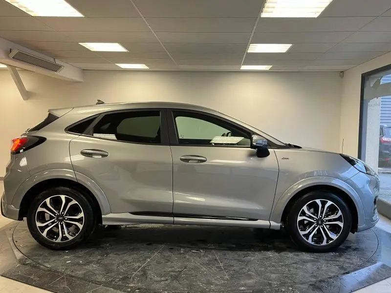 Vue de profil côté gauche d'un Ford Puma gris Solar métallisé avec jantes alliage et vitres arrière surteintées dans un showroom.