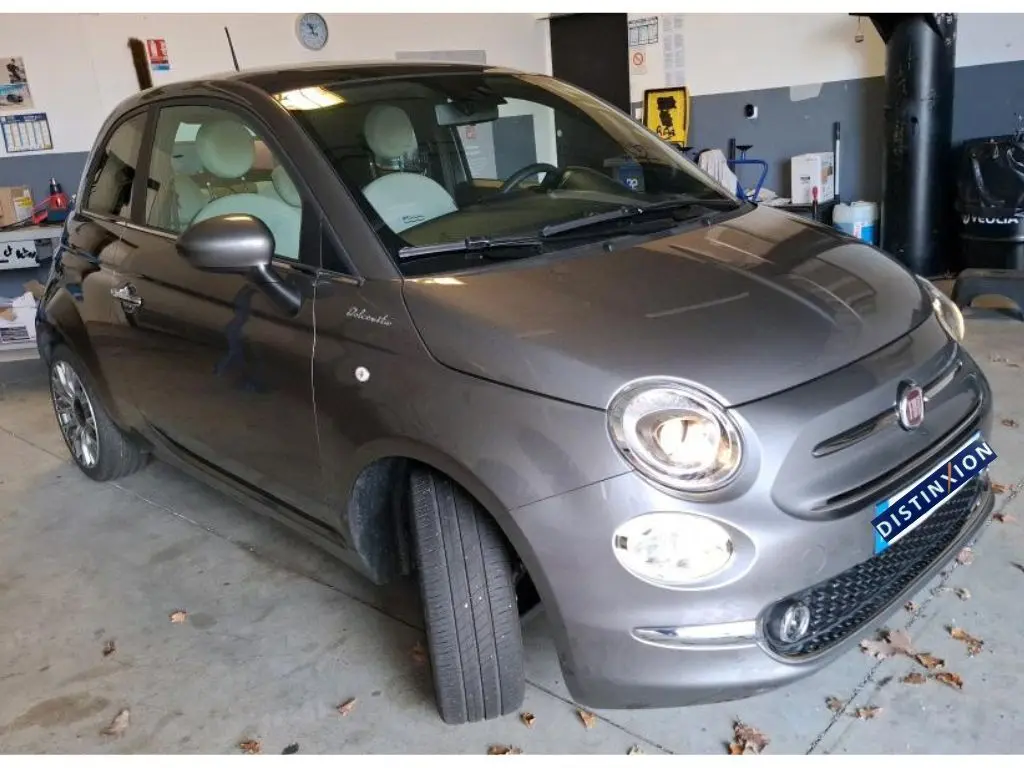 Vue 3/4 avant droit d'une FIAT 500 gris Electroclash avec phares allumés, stationnée en intérieur.
