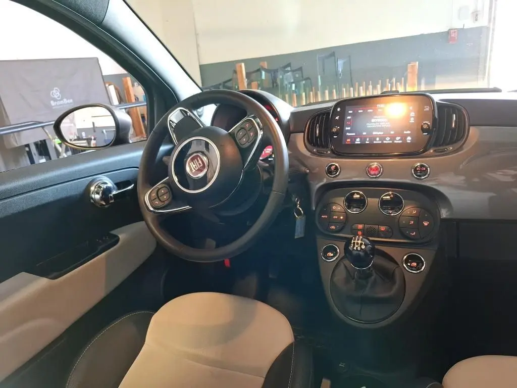 Intérieur du Fiat 500 2022 vu côté conducteur, tableau de bord gris Electroclash avec écran tactile et levier de vitesse manuel.