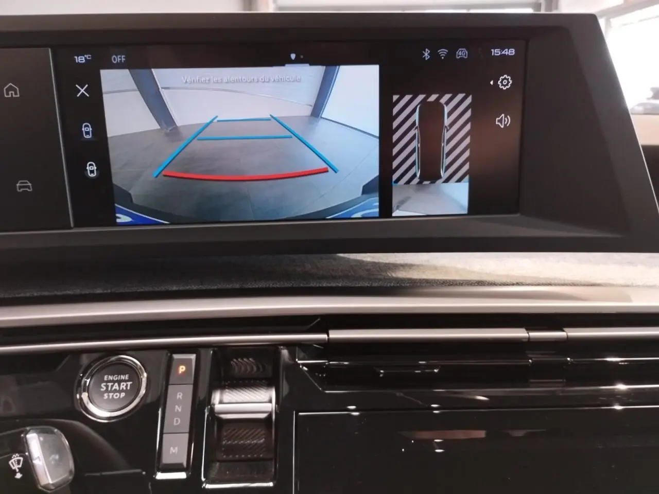 Vue intérieure du tableau de bord du Peugeot 5008 Hybrid 2025, écran de caméra de recul et commandes de boîte auto visibles.