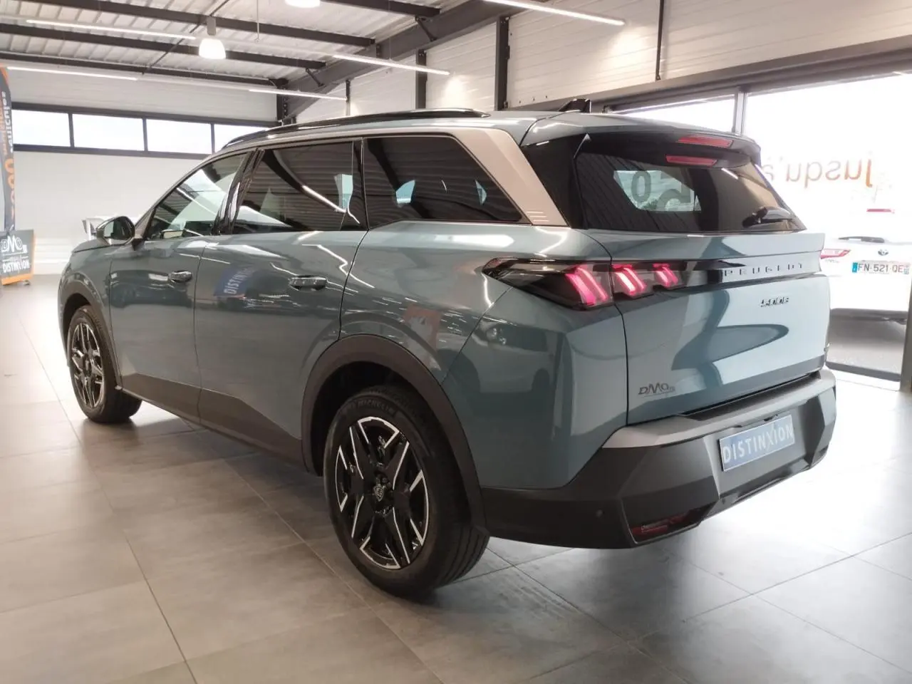 Vue 3/4 arrière droite du Peugeot 5008 hybride Bleu Ingaro avec jantes alliage noires et feux arrière LED 3 griffes allumés.